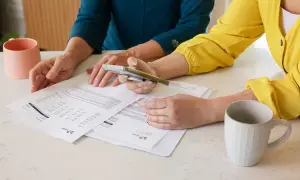 Dwie kobiety analizują dokumenty, dyskutując o tym, co to jest pełnomocnictwo. Na stole stoją kubki.
