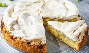 Ein saftiger Stachelbeer Baiser Kuchen mit goldbraunem Boden und fluffiger Baiserhaube, ein Stück ist angeschnitten.