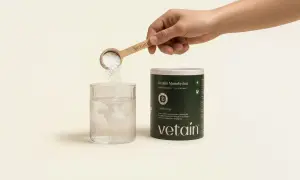 Eine Hand schüttet Kreatinpulver aus einem Löffel in ein Glas Wasser. Das Pulver löst sich auf, was auf die Einnahme von Kreatin hindeutet, das manchmal mit Wassereinlagerung in Verbindung gebracht wird.