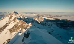 Słoneczny poranek na Kozi Wierch zimą. Śnieg lśni na zboczach, a w dole morze chmur.