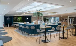 Un espace restauration moderne avec un bar bleu, des tabourets gris, une plante tropicale et des tables rondes.