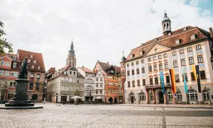 Blick über den Marktplatz der Coburg Altstadt mit historischen Gebäuden, einem Denkmal und Fahnen.
