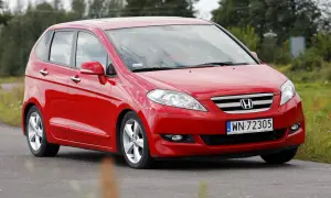 Czerwona Honda FR-V jedzie po drodze, otoczona zielenią.