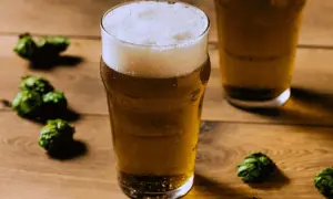 Un bicchiere di birra dorata con schiuma abbondante, circondato da luppoli verdi su un tavolo di legno. Perfetto per una festa della birra!