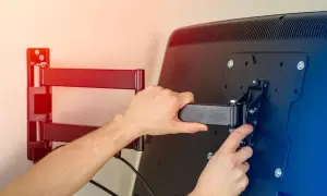 Montaż telewizora na ścianie. Ręce przykręcają uchwyt do ekranu, przygotowując mocowanie telewizora na ścianie.