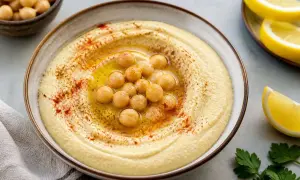 Houmous sans tahini crémeux, garni de pois chiches, d'huile d'olive et de paprika. Servi avec des quartiers de citron.