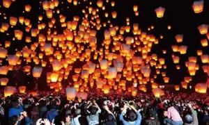 Tysiące lampionów unosi się na nocnym niebie, tworząc magiczny widok podczas święta lampionów. Tłum ludzi obserwuje to widowisko.