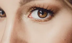 Un œil marron orné d'un maquillage soirée doré scintillant, parfait pour briller toute la nuit.