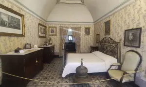 Camera da letto nella casa di d'Annunzio, con carta da parati floreale, letto in ferro battuto e mobili d'epoca.