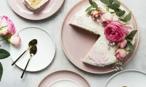 Jak zabezpieczyć kwiaty do tortu? Różowy tort ozdobiony różami i eukaliptusem, obok talerze z kawałkami ciasta i złote łyżeczki.