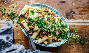 En skål med rig pasta lenticchie, toppad med färska örter och riven ost, serverad på ett rustikt träbord.