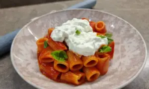 Rigatoni al sugo con abbondante stracciatella cremosa e basilico fresco. Un piatto semplice ma delizioso.