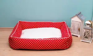 Rotes Hundebett mit weißen Punkten und weißer Liegefläche, bereit fürs hundebett waschen. Daneben stehen Deko-Häuschen.