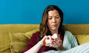 Vrouw neemt medicatie, hopend dat werkt bachbloesem echt. Ze zit op een bank met een deken.