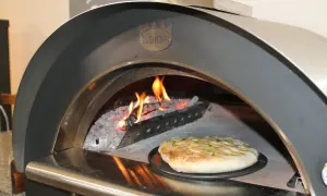 Una crescia dorata pronta per essere infornata in un forno a legna Clementi, con fiamme vive che creano l'atmosfera perfetta per la ricetta.