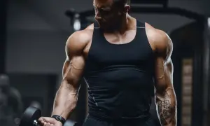 Ein Mann mit beeindruckenden **Armmuskeln** hebt eine Hantel im Fitnessstudio. Seine Bizeps und Unterarme sind stark definiert.