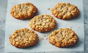 Fem gyllene glutenfria havrekakor ligger på bakplåtspapper. Perfekta för alla fika-stunder.