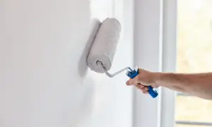 Mano aplica pintura aterciopelada blanca a una pared con un rodillo.