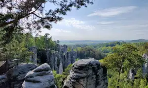 Blick über die Prachauer Felsen, eine beeindruckende Sandsteinformation, umgeben von grünen Wäldern und einem weiten Horizont unter blauem Himmel.