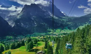 Widok z kolejki linowej na dolinę Grindelwald, z górami w tle i zielonymi łąkami.