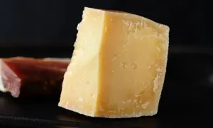 Kawałek twardego, żółtego parmezanu, idealny na przekąskę w ciąży. Obok kawałek wędliny.