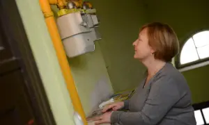 Kobieta sprawdza, gdzie jest numer licznika gazu, który znajduje się na żółtej rurze obok liczników.