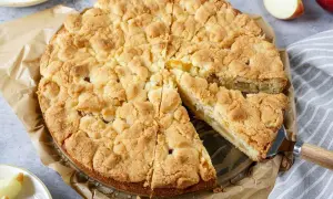 Ein goldbrauner Apfelkuchen mit Streuseln, ein Stück wird gerade herausgehoben.