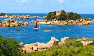 Un voilier navigue près d'un château sur une île rocheuse en Bretagne. Le paysage est typique de la côte bretonne.