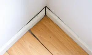 Esquina de habitación con suelo laminado hinchado por agua, mostrando las tablas separadas y levantadas.
