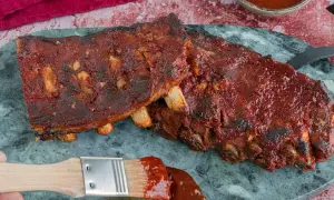 Saftige Spareribs sous vide, glasiert mit BBQ-Sauce. Ein Pinsel mit Sauce liegt daneben.