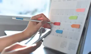 Ręka z ołówkiem zaznacza na kalendarzu dni wolne od pracy. Planowanie urlopu.