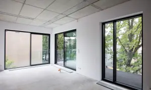 Wnętrze w stanie surowym zamkniętym, z betonowym sufitem i betonową podłogą. Duże okna wychodzą na zieleń. To początek drogi do stanu deweloperskiego.