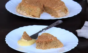 Una fetta di torta nocciole piemontese originale, soffice e dorata, servita con crema gialla.