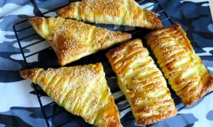 Chrupiące ciasto francuskie z serem, posypane sezamem, prezentuje się apetycznie na czarnej kratce.
