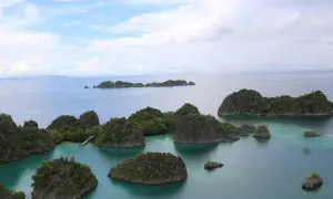Grüne Inseln ragen aus türkisfarbenem Wasser, eine malerische Aussicht, die man vom Raja Ampat Flughafen aus genießen kann.