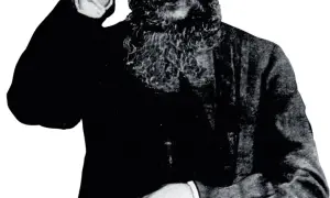 Grigorij Rasputin, z charakterystyczną brodą, wznosi rękę w geście błogosławieństwa lub pozdrowienia.