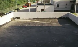 Płaski dach z widocznym odpływem, gotowy na deszcz. W tle budynki i drzewa.