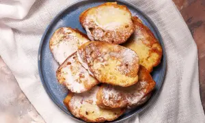 Armer Ritter, goldbraun gebacken und mit Puderzucker bestäubt, liegen auf einem blauen Teller.