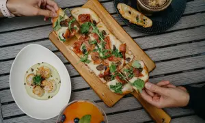 Pizza wegetariańska z figami i rukolą, obok talerz z przegrzebkami i drink.
