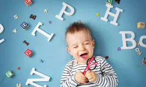 Uśmiechnięte dziecko z okularami, otoczone literkami. Radość, gdy dziecko zaczyna mówić pierwsze zdania.