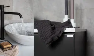 Svart blandare som rinner ner i ett marmorerat handfat. En mörk handduk ligger på ett svart skåp. Det ser ut som att någon ska montera handfatet.