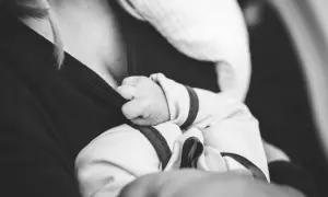 Dłoń noworodka czepia się ubrania mamy. Delikatne paluszki, mimo chwilowych baby blues, szukają bliskości.