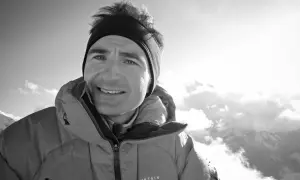 Ueli Steck, lächelnd in warmer Bergkleidung, blickt in die sonnige, wolkenverhangene Bergwelt.