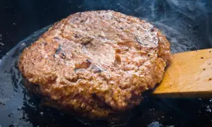 Jugosa carne dorándose en sartén, parte de como hacer hamburguesas caseras. Humo y burbujas de grasa.