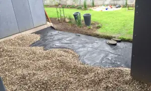 Baustelle für eine splitt terrasse mit Vlies und Kies. Im Hintergrund Rasen und Spielzeug.