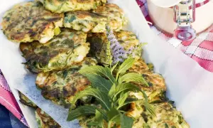 Gestapelte, goldbraune Zucchini Frikadellen, garniert mit frischen Kräutern und lila Blüten. Ein köstlicher Sommergenuss.