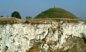 Krakus mound, zielona kopuła z dwiema postaciami na szczycie, góruje nad wapiennym klifem.