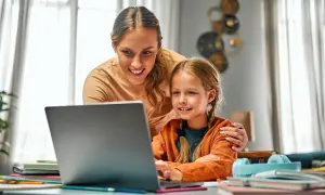 Uśmiechnięta mama wspiera córkę w nauce przy laptopie. To piękny przykład opieki na dziecko, wspólnego spędzania czasu i wspierania rozwoju.