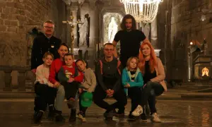 Rodzina zwiedza kopalnię soli w Wieliczce. Dzieci z rodzicami siedzą na ławce w podziemnej kaplicy, podziwiając solne rzeźby i żyrandol.