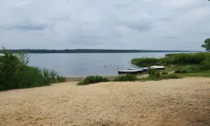 Piaszczysta plaża nad Zalewem Porajskim, z kilkoma łódkami przy brzegu. Idealne miejsce na wypoczynek i podziwianie przyrody.
